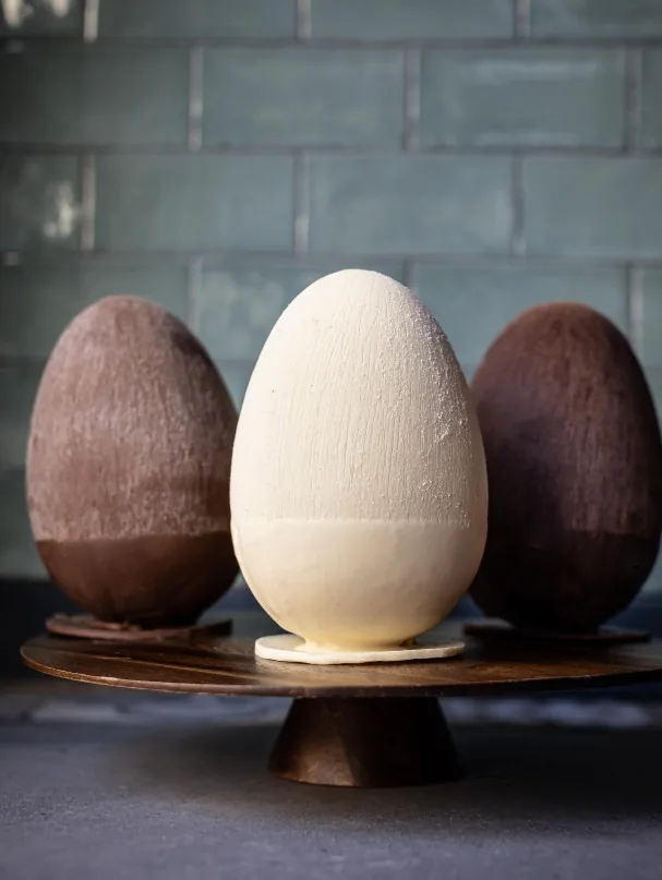 Trois œufs de Pâques en chocolat lait, blanc et noir sur un présentoir
